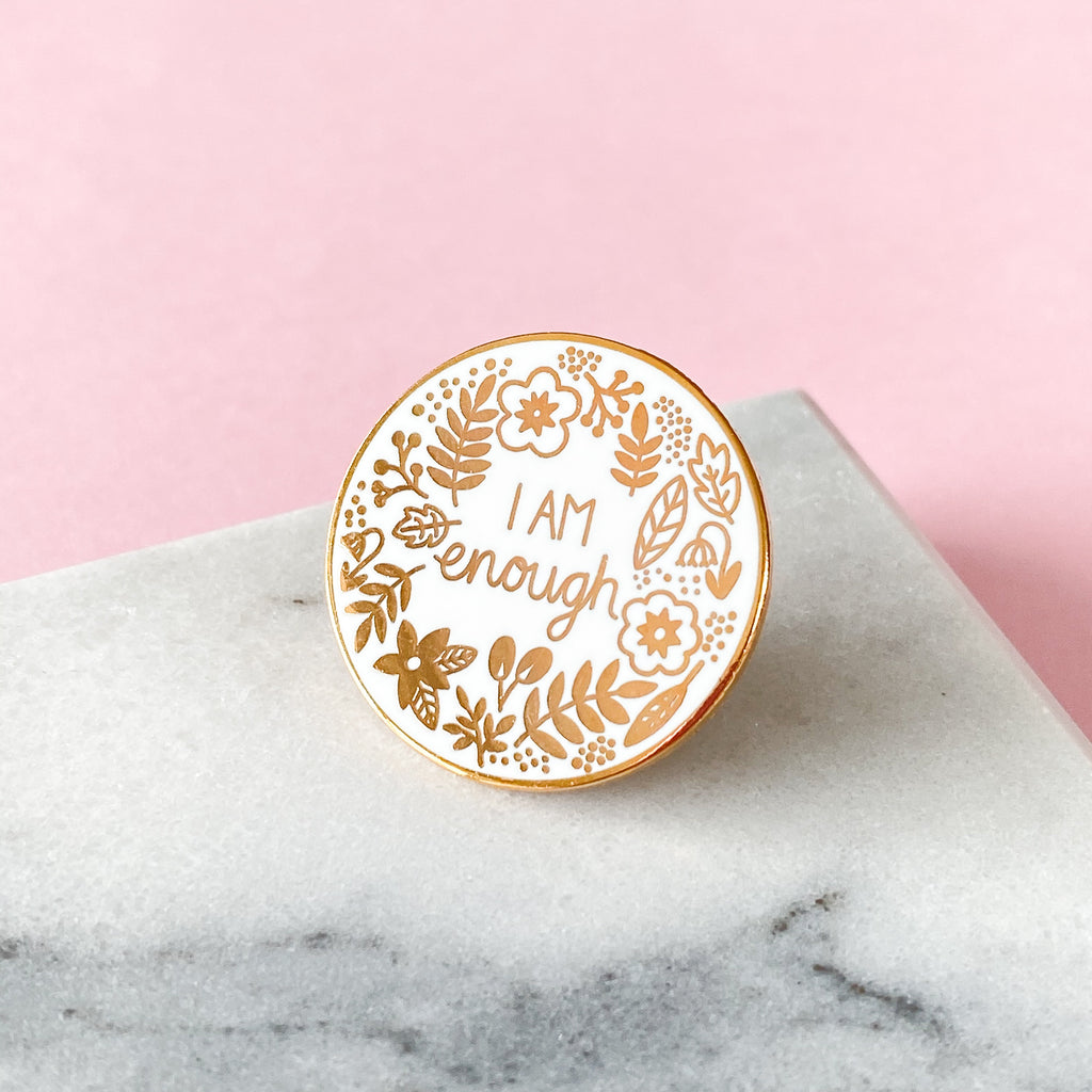 An enamel pin in rose gold which states I am enough.